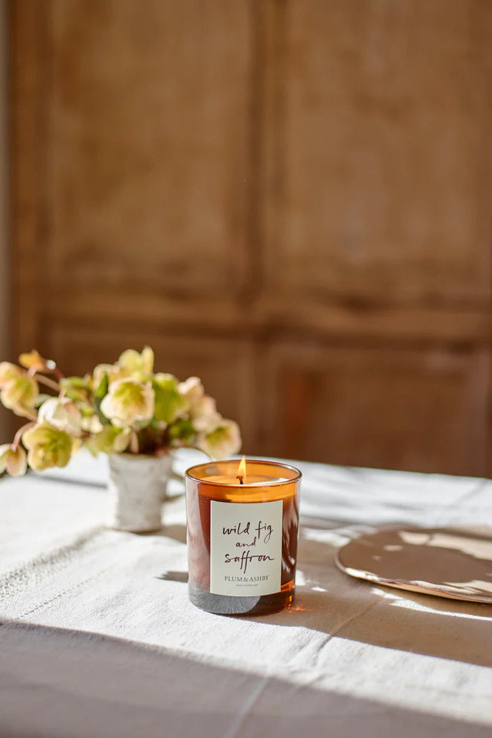 Candle with a label on a table with flowers and cutlery in the background