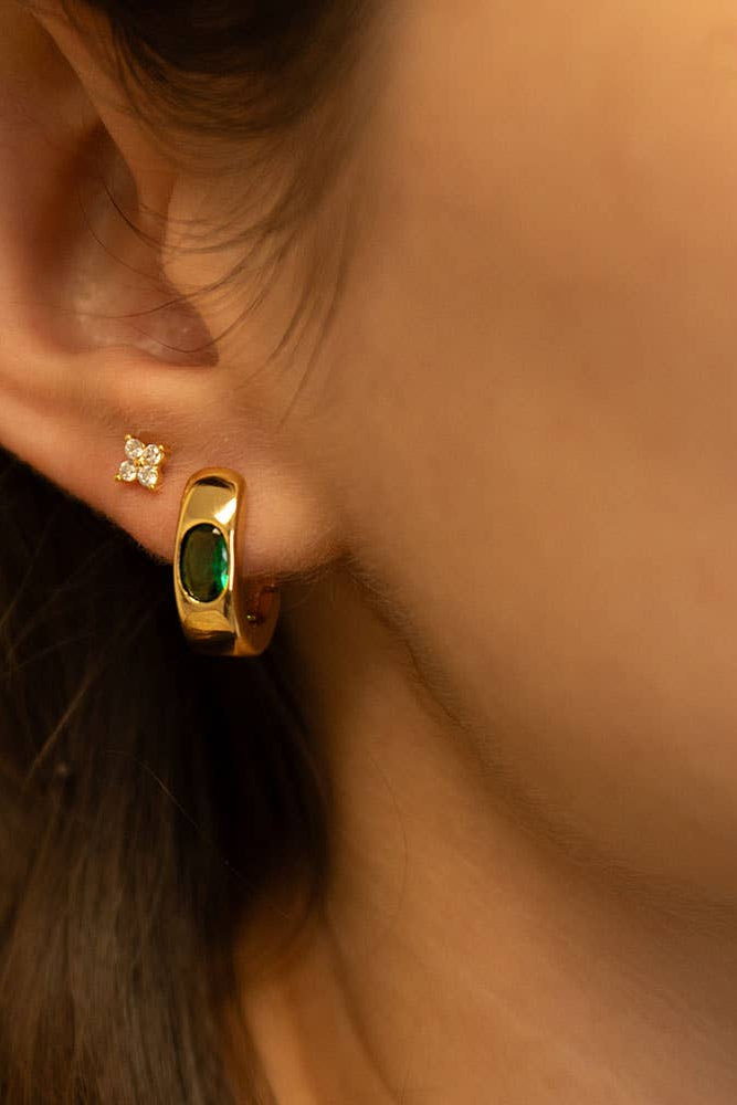 Close-up of a person wearing a gold earring with a green gemstone.