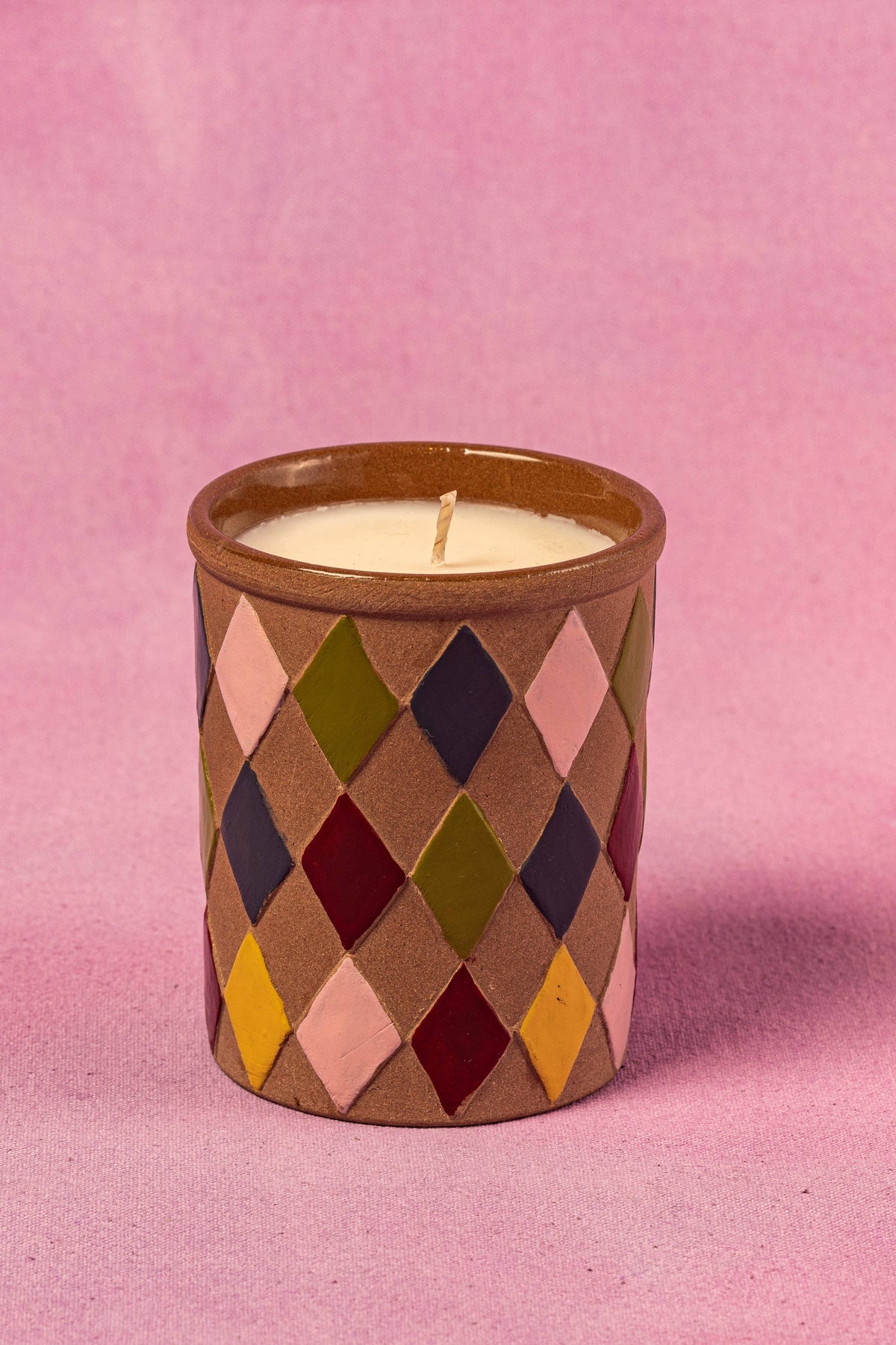 Candle in a diamond patterned container on a pink background