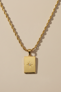 Gold necklace with a rectangular pendant on a beige background