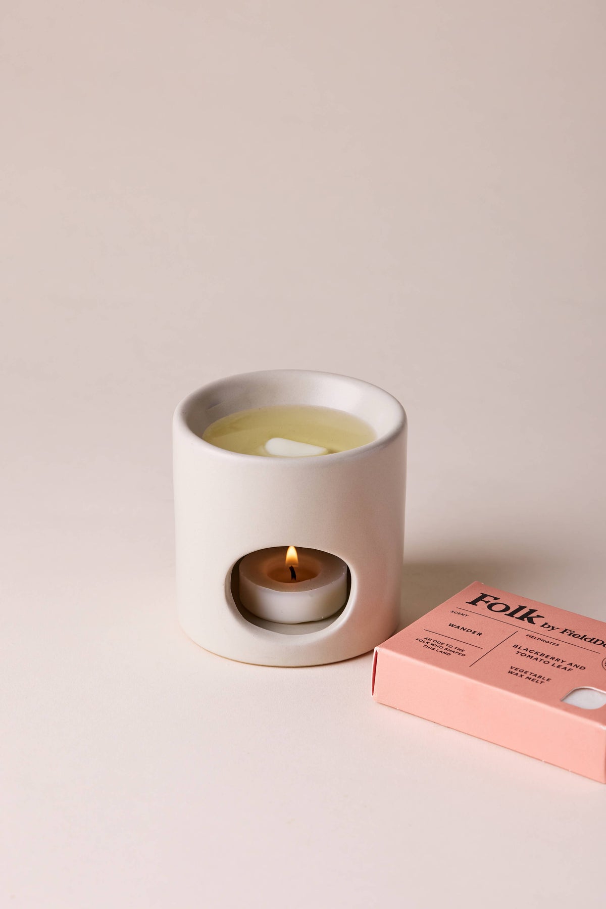 Ceramic wax warmer with a lit candle and a pink box labeled 'Folk' on a beige background