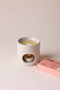 Ceramic wax warmer with a lit candle and a pink box labeled 'Folk' on a beige background