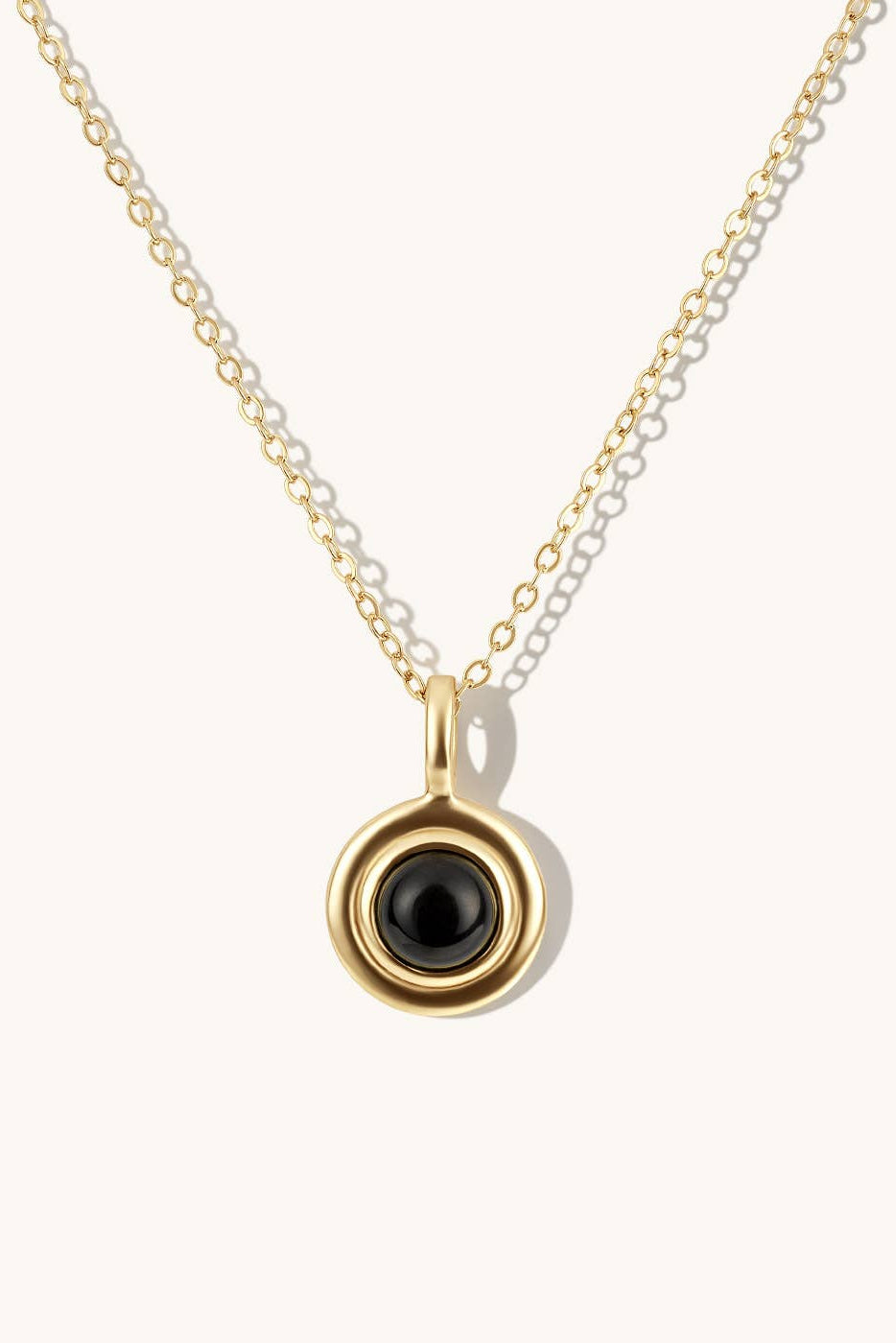 Gold necklace with a black pendant on a white background