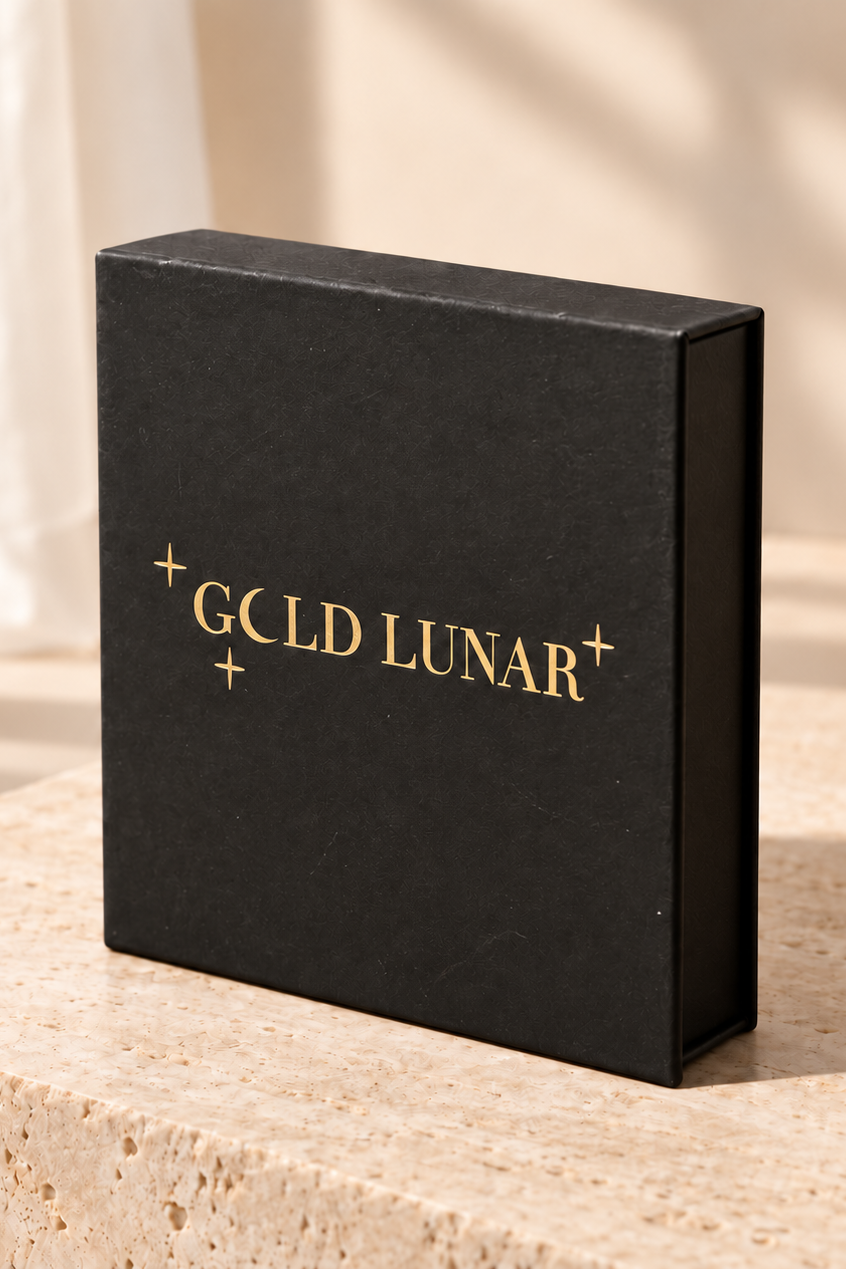 A black rectangular gift box with gold foil text reading 'GCLD LUNAR' and small star accents, standing on a beige stone surface in warm natural light.