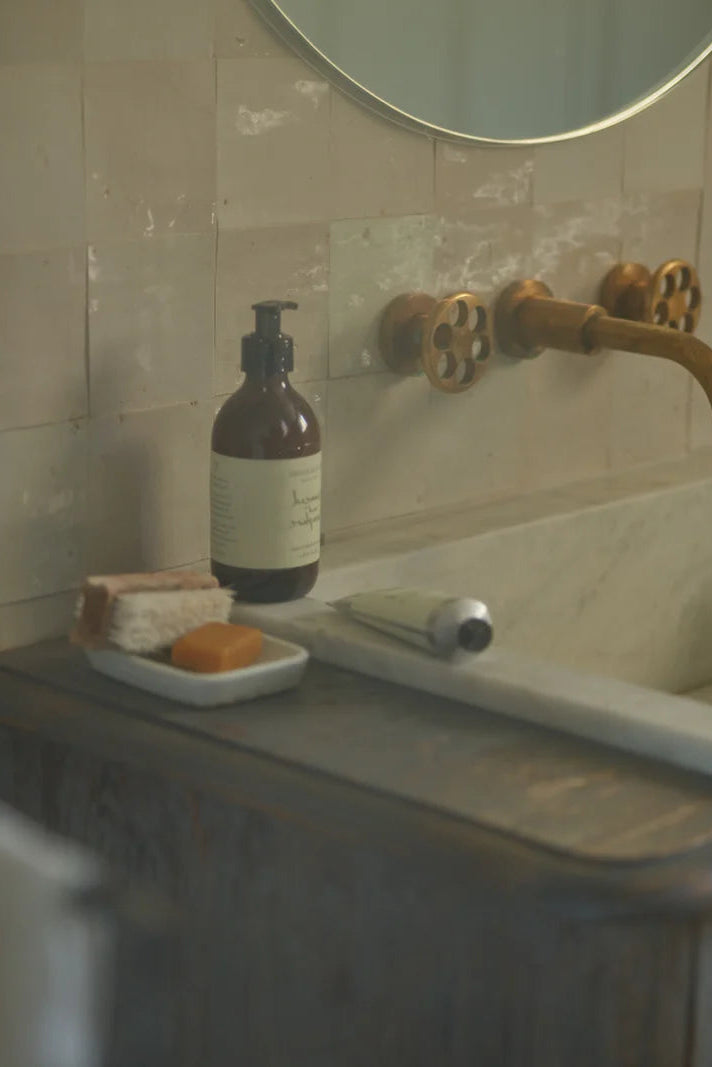 Bottle of soap on a soap dish next to a sink with a gold faucet.