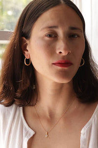 Woman wearing gold hoop earrings and a necklace indoors with a window in the background