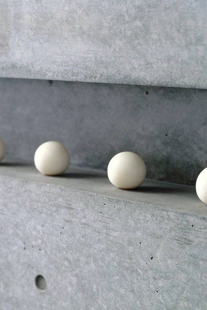 Four white spherical objects on a concrete surface with a concrete wall in the background