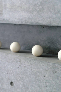 Four white spherical objects on a concrete surface with a concrete wall in the background