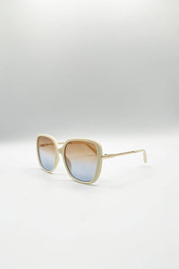 A pair of oversized square sunglasses with a cream-colored frame and gradient lenses that transition from a warm brown at the top to a light blue at the bottom, displayed on a clean white studio background.