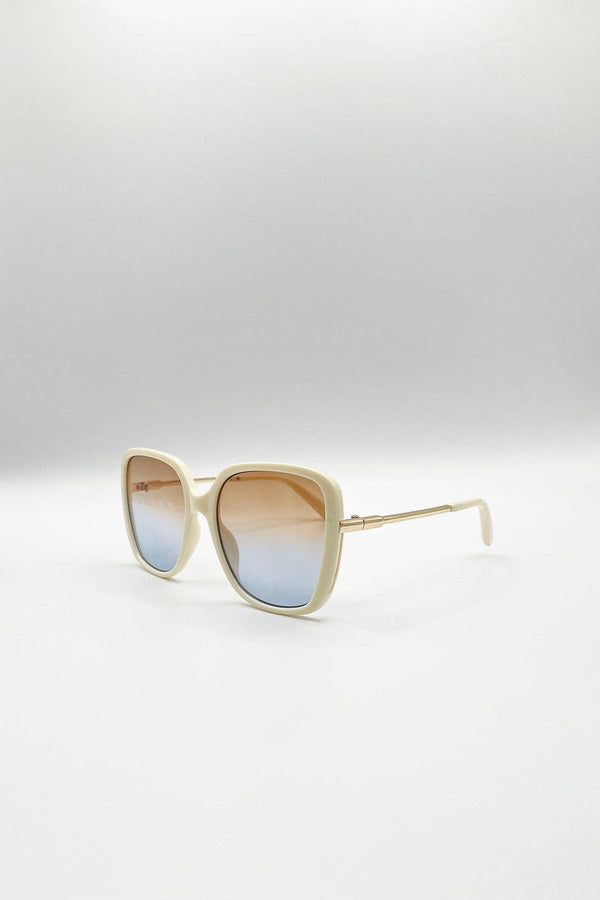 A pair of oversized square sunglasses with a cream-colored frame and gradient lenses that transition from a warm brown at the top to a light blue at the bottom, displayed on a clean white studio background.