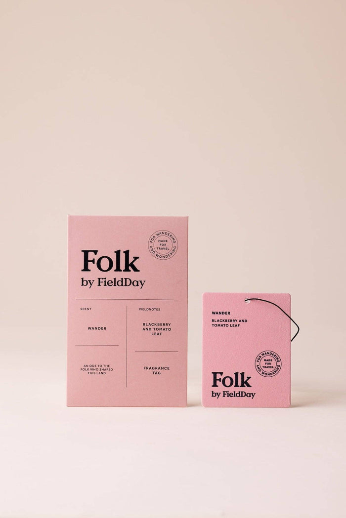 Pink packaging for Folk by FieldDay fragrance, showing a tall rectangular box and a smaller hanging tag on a plain warm beige background.