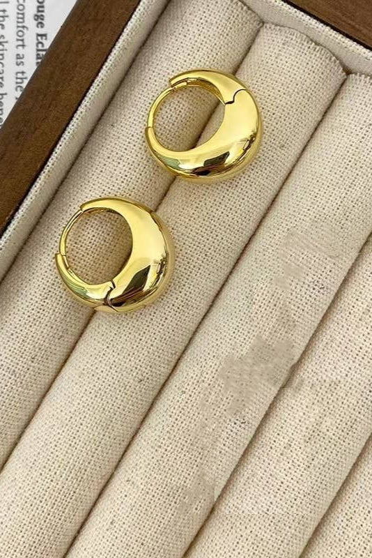 Gold hoop earrings on a beige fabric surface with a wooden box.