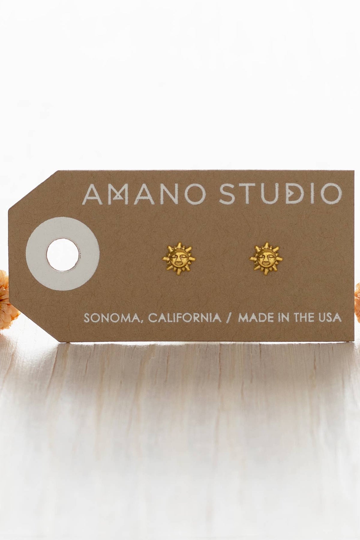 Gold sun-shaped earrings on a 'Amano Studio' branded card with 'Sonoma, California' and 'Made in the USA' text.