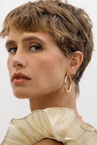 Woman with short hair wearing gold hoop earrings against a plain background
