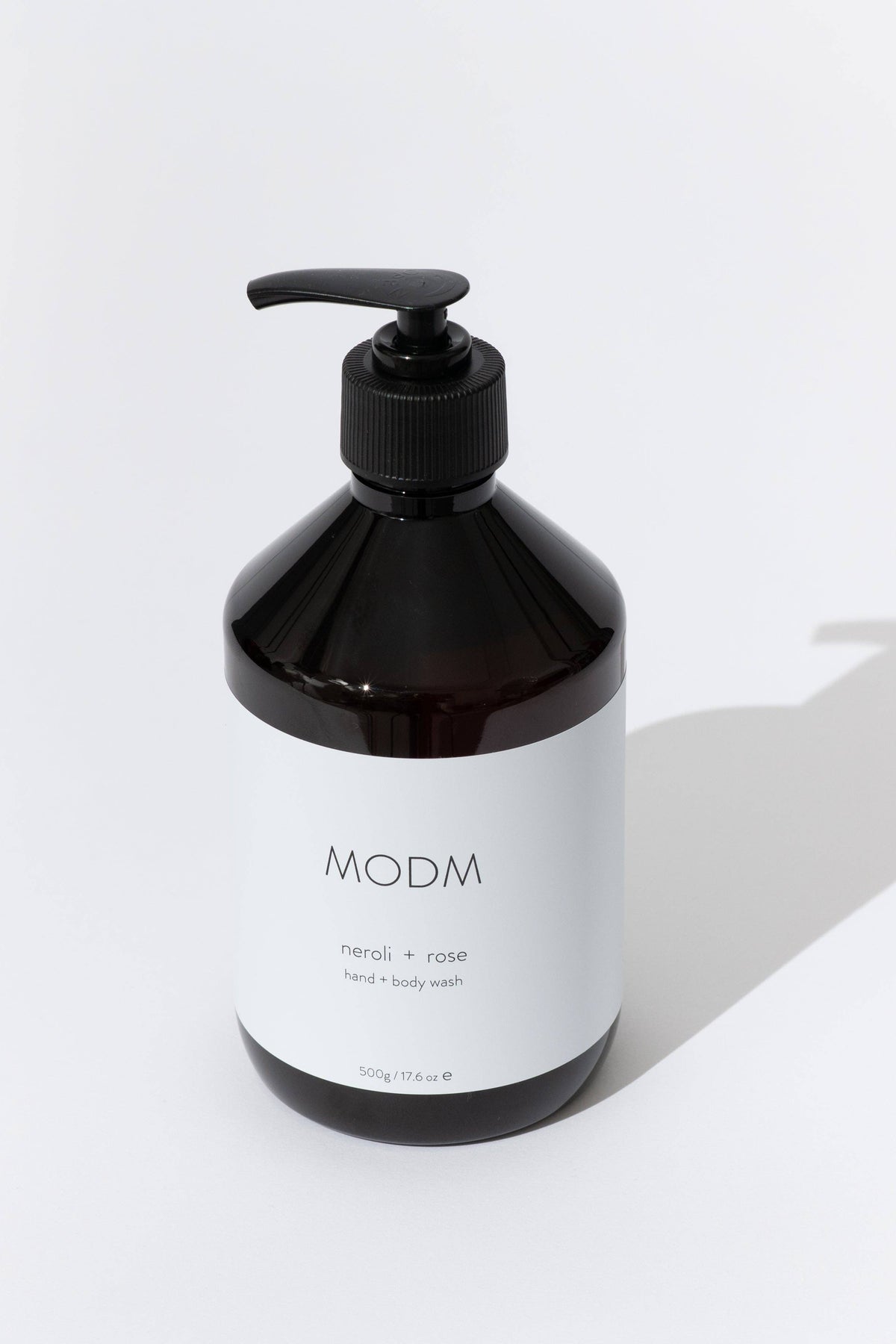 A dark amber pump bottle of MODM body wash with a white label, set against a clean white background with a soft shadow.