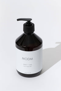 A dark amber pump bottle of MODM body wash with a white label, set against a clean white background with a soft shadow.