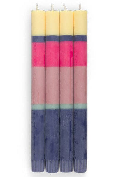 Four striped taper candles standing upright, featuring horizontal bands of pale yellow, dark navy, bright pink, dusty rose, and light blue on a white background.