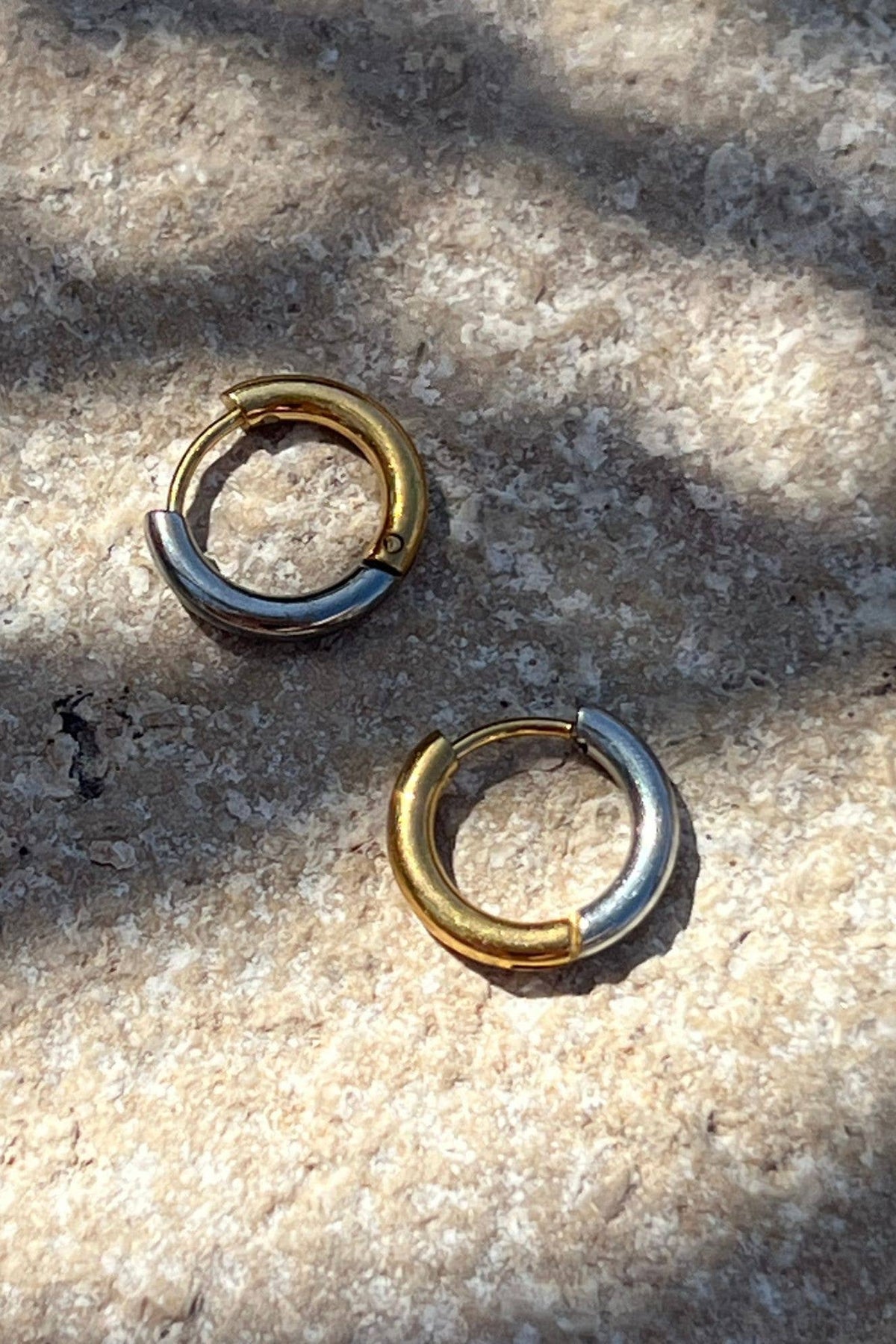 Two gold and silver hoop earrings on a textured stone surface