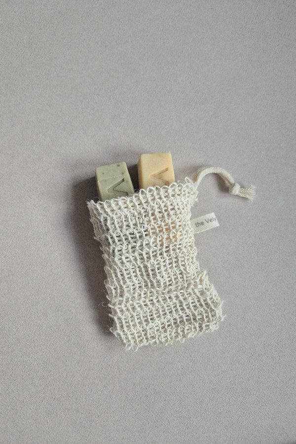 Two bars of soap in a natural fiber bag on a gray background