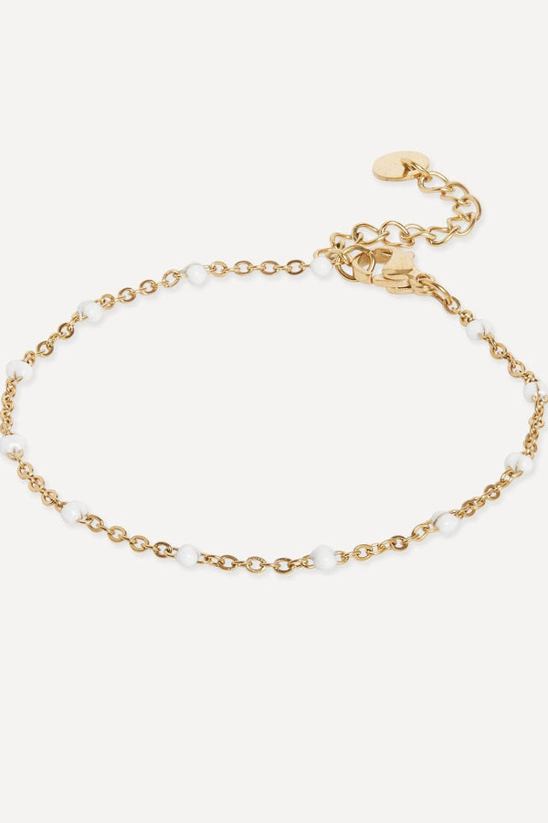 A delicate gold chain bracelet with small white pearl beads spaced along the chain, featuring a lobster clasp and an adjustable extension chain with a small round tag, shown on a light off-white background.