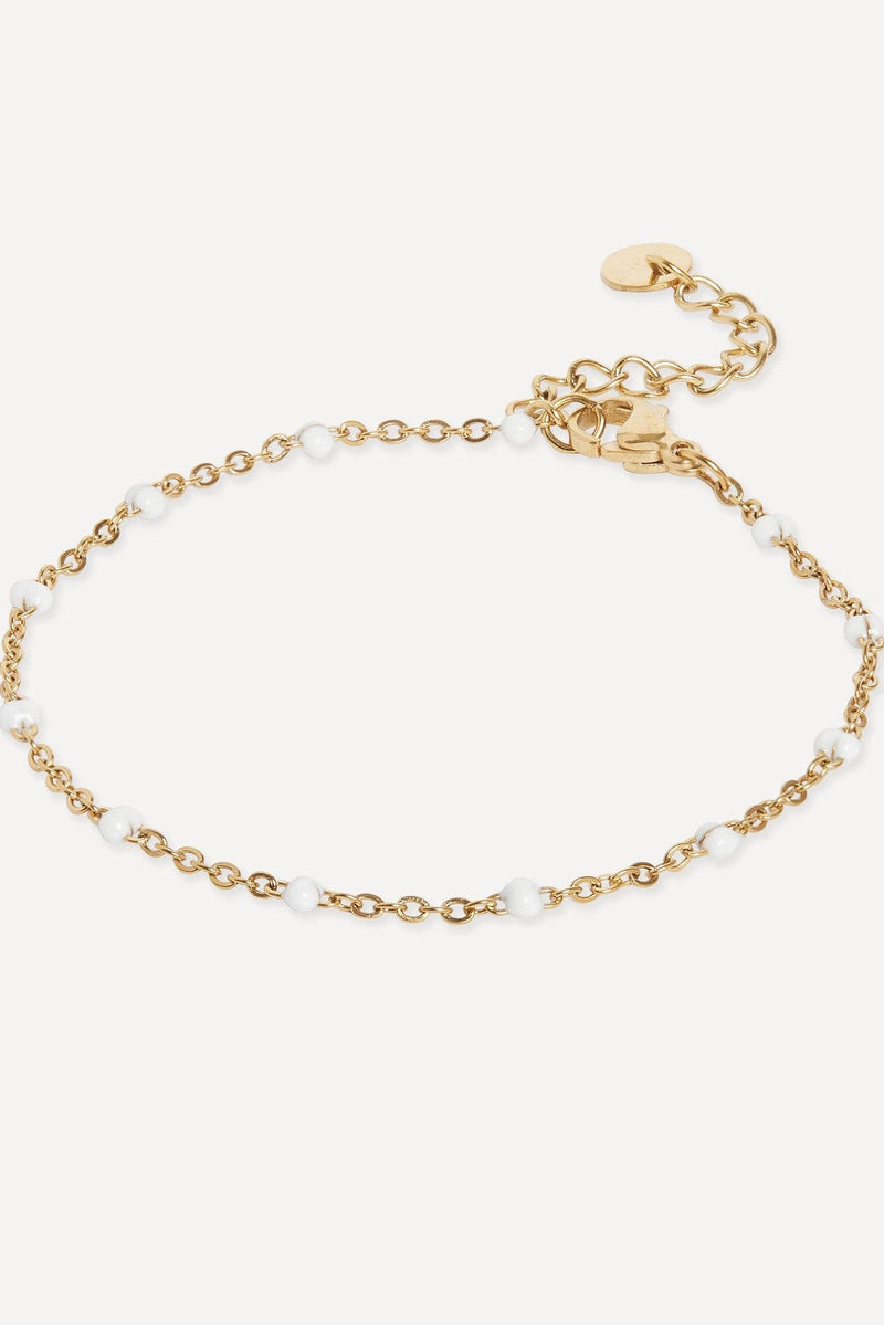 A delicate gold chain bracelet with small white pearl beads spaced along the chain, featuring a lobster clasp and an adjustable extension chain with a small round tag, shown on a light off-white background.