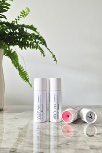 Three Vely lip balm containers on a marble surface with a plant in the background