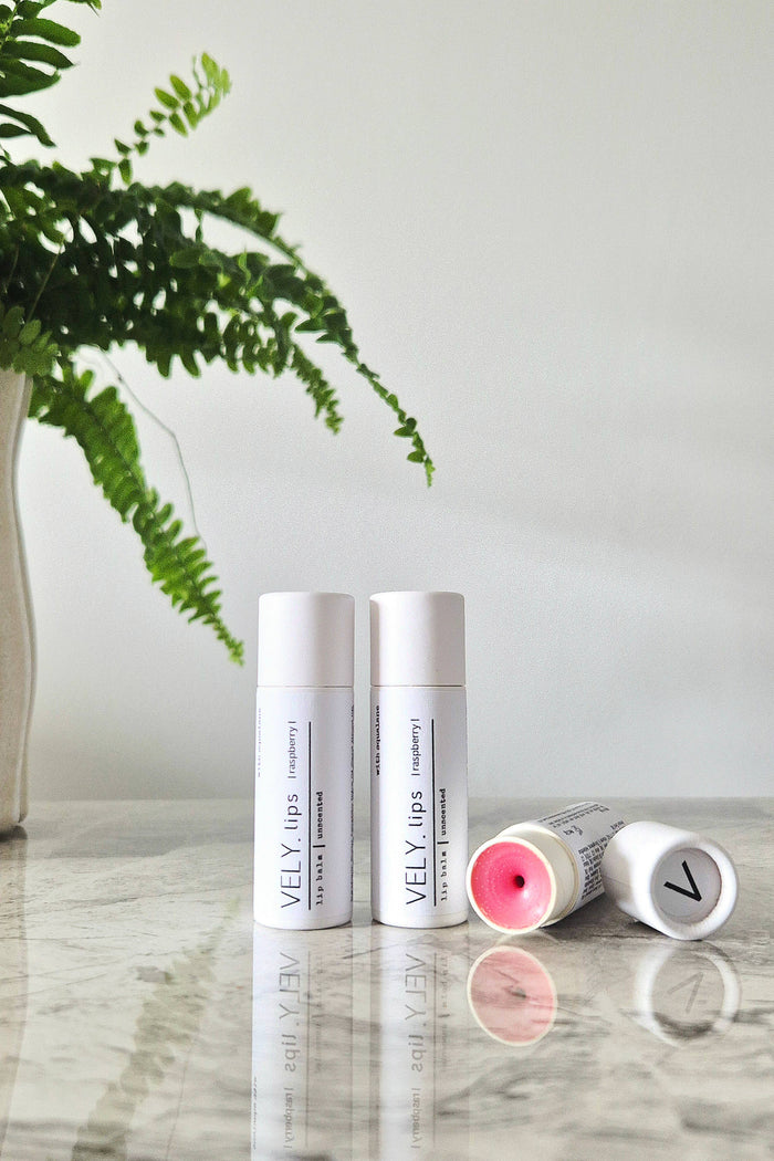Three Vely lip balm containers on a marble surface with a plant in the background