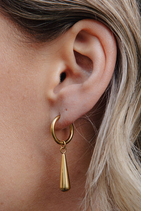 Close-up of an ear wearing a gold hoop earring with a dangling teardrop design.