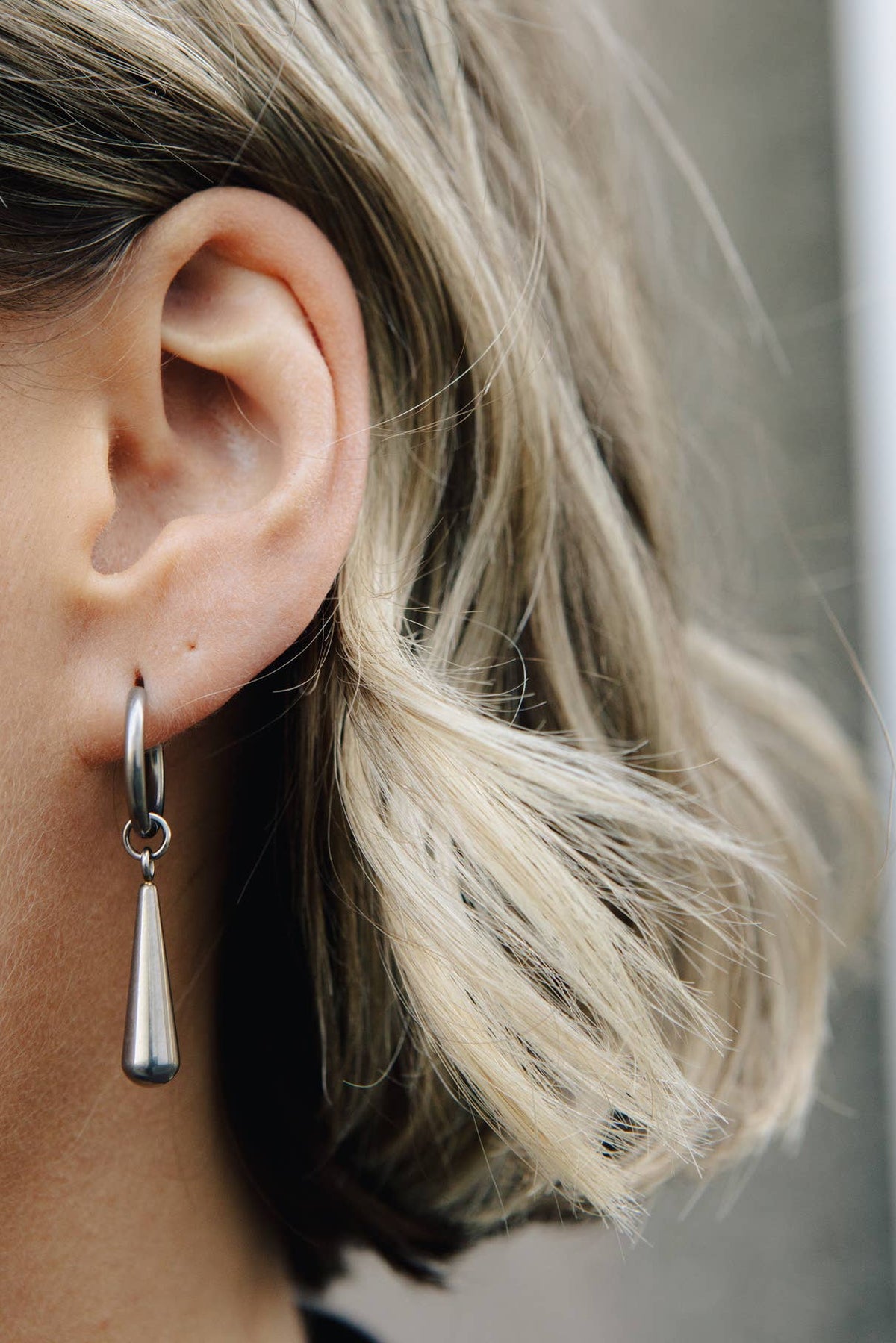 Close-up of an ear wearing a silver hoop earring with a dangling teardrop charm.