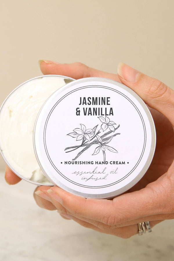 Hand holding a jar of Jasmine & Vanilla hand cream with a beige background