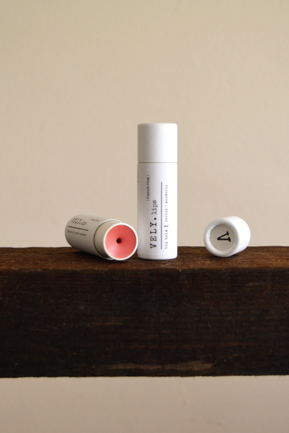 Three lip balm tubes on a wooden shelf with a neutral background