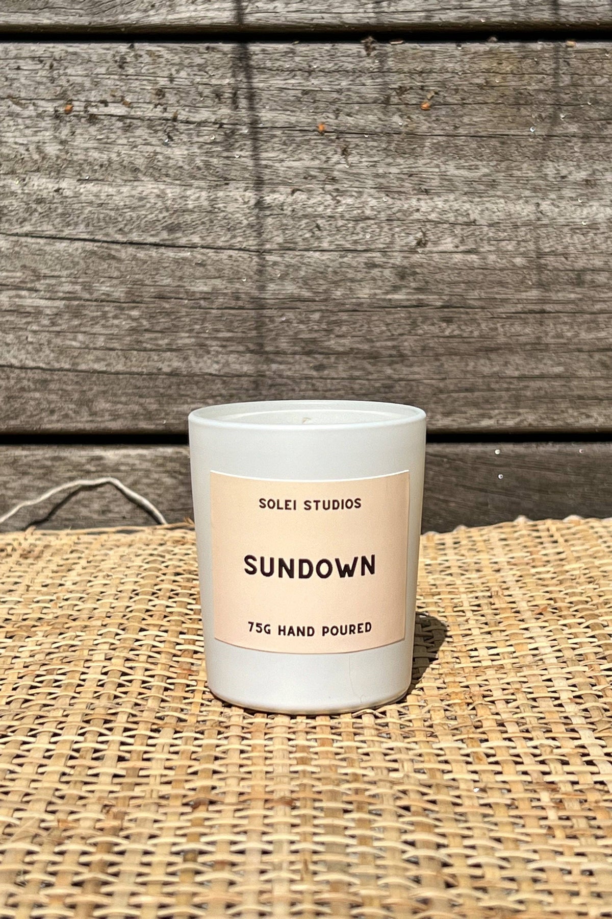 Candle labeled 'Sundown' by Solei Studios on a woven surface with wooden background