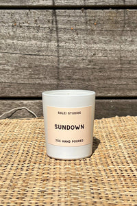 Candle labeled 'Sundown' by Solei Studios on a woven surface with wooden background
