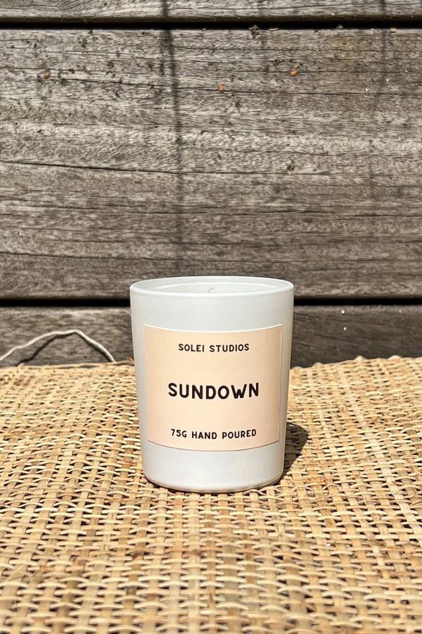 Candle labeled 'Sundown' by Solei Studios on a woven surface with wooden background