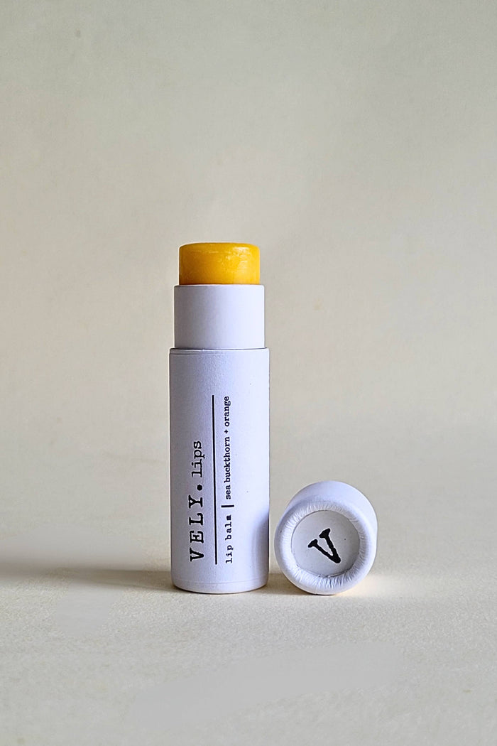 White lip balm stick with yellow cap and visible branding on a light gray background