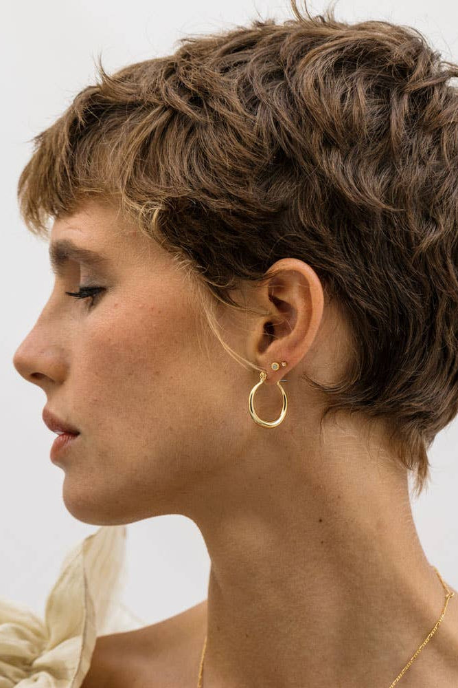 Woman with styled short hair wearing gold hoop earrings against a neutral background