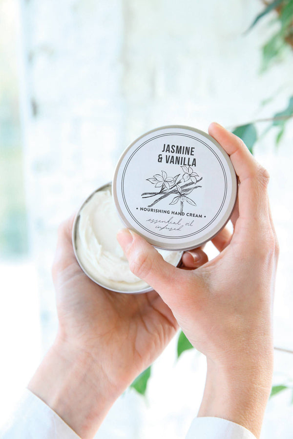 Hand holding a jar of Jasmine & Vanilla hand cream with a blurred natural background