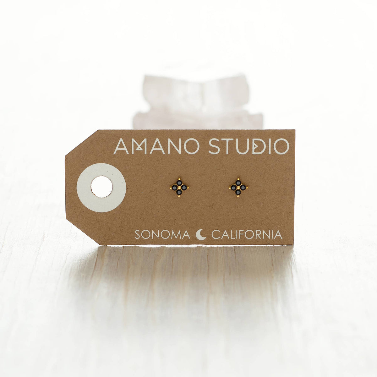 Earring card with earrings on a white background, featuring 'Amano Studio' branding.