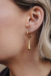 Gold hoop earring with a dangling teardrop on an ear