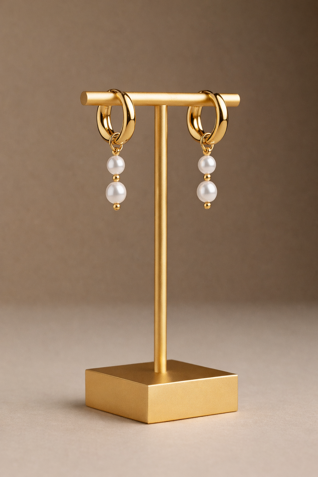 Gold hoop earrings with pearl beads on a gold stand against a brown background