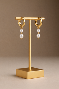 Gold hoop earrings with pearl beads on a gold stand against a brown background