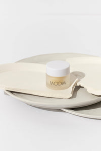 Cosmetic container with 'MODM' branding on a white surface