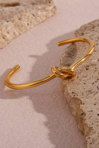 Gold bracelet with knot design on a textured stone surface