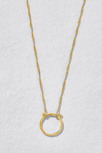 A delicate gold chain necklace featuring a large, textured open circle pendant, displayed against a light gray textured background.