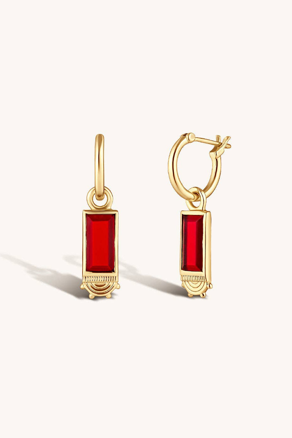 A pair of gold hoop earrings with rectangular red gemstone charms, displayed on a clean off-white background.