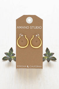 Gold hoop earrings on a 'Amano Studio' branded card with succulents in the background.