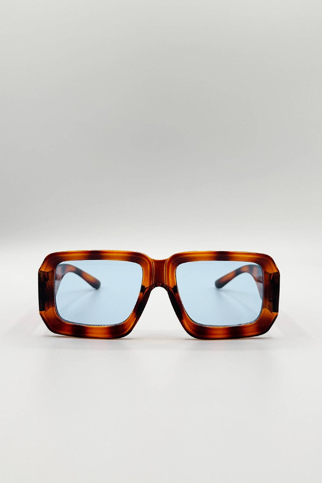 Sunglasses with tortoiseshell frame and blue lenses on a light gray background