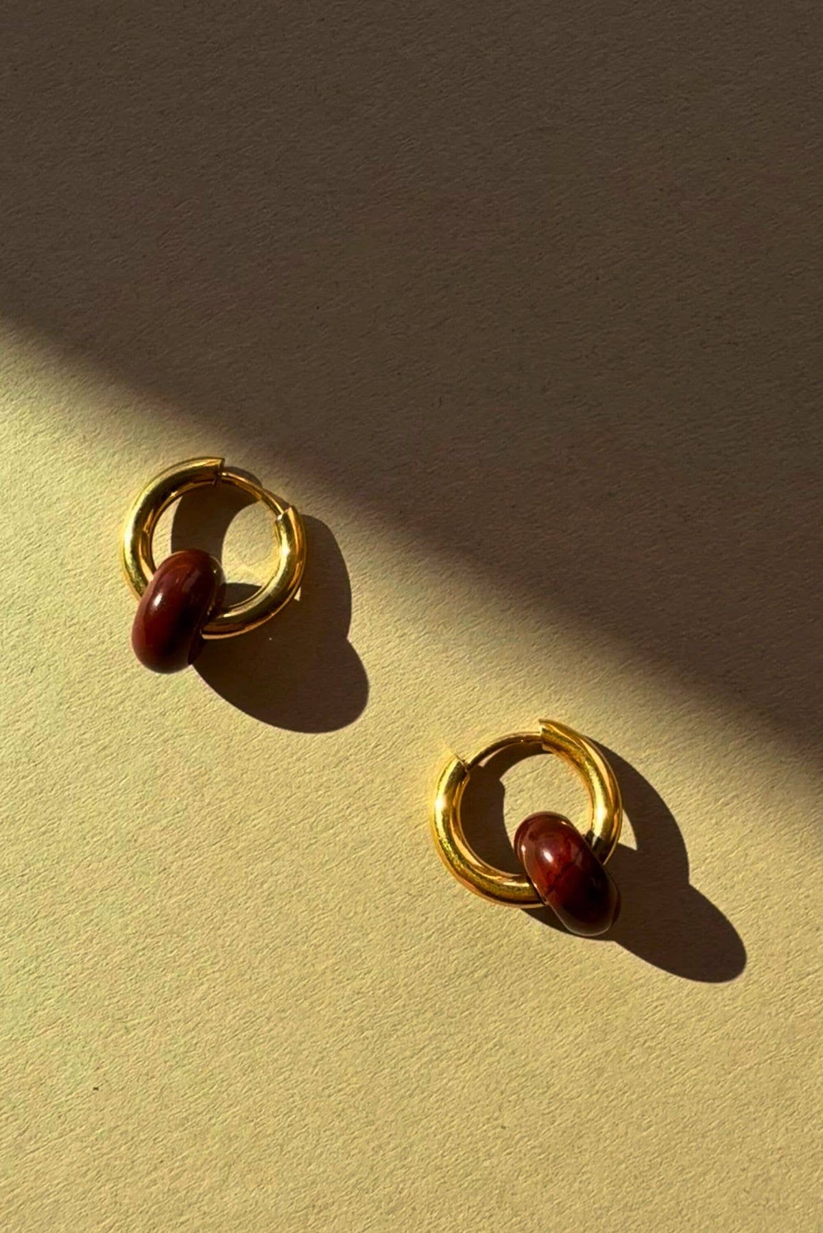 Gold hoop earrings with a central red gemstone on a beige surface.