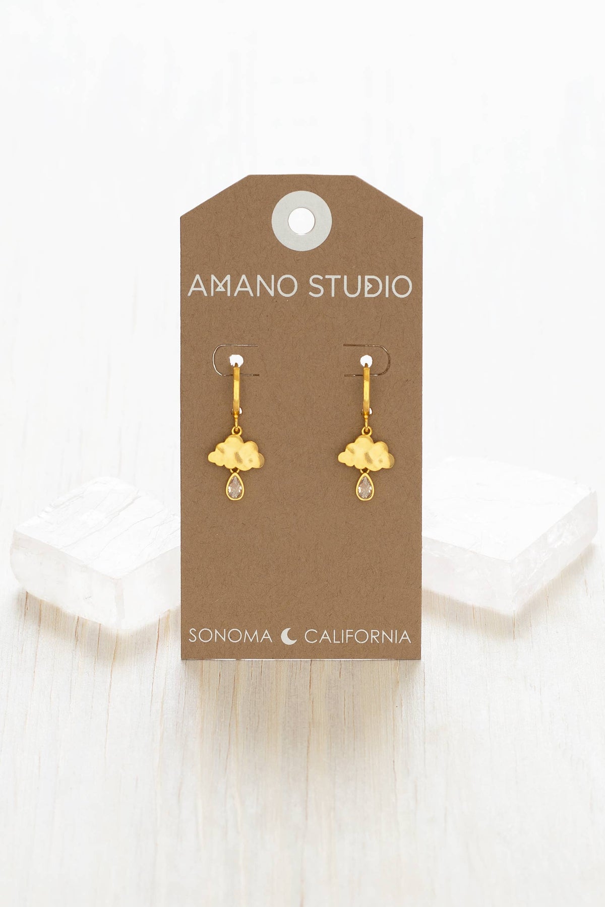 Gold earrings on a 'Amano Studio' branded card with a white background