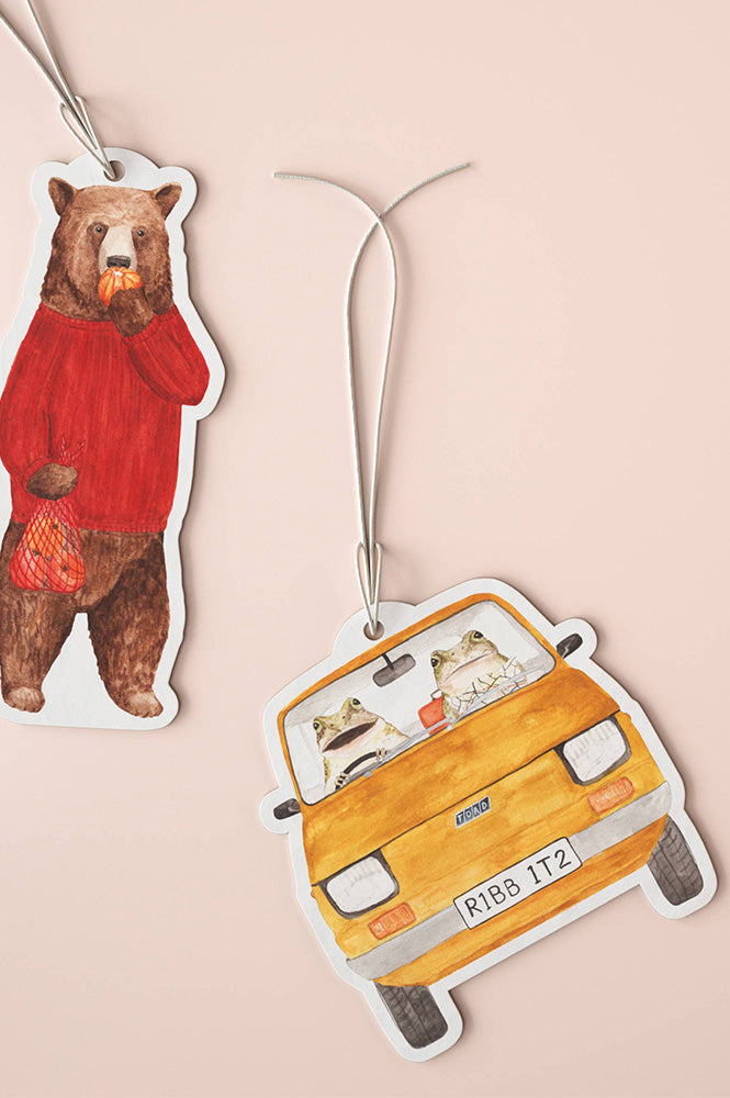 Car air freshener with a bear in a red sweater and two frogs in a car on a pink background